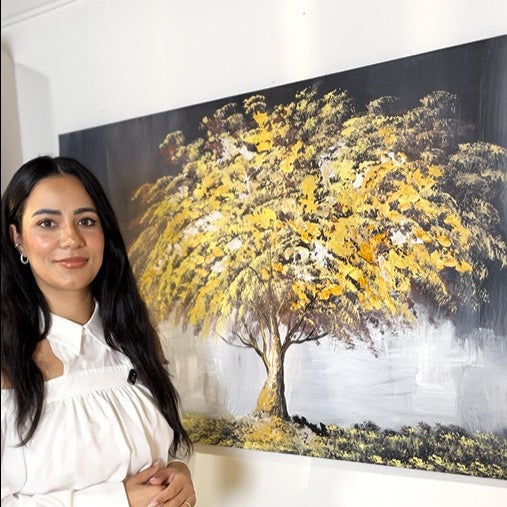 Woman standing next to a painting of a tree with yellow leaves on a white wall.